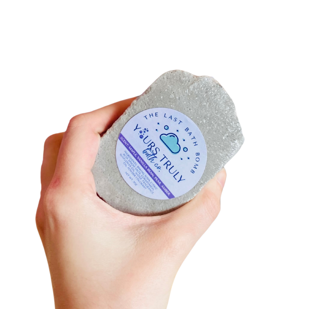 Hand holding a gray bath bomb with a label on a white background